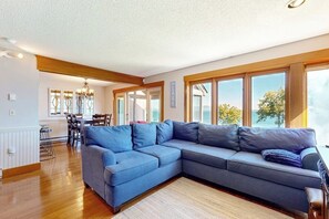 Ein modernes Wohnzimmer mit einem großen, L-förmigen Ecksofa, einem Essbereich mit Tisch und Stühlen und großen Fenstern mit Blick.