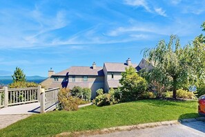 Ein Wohnhaus mit einem gepflegten Rasen, einer Holzterrasse und freiem Blick auf die umliegende Landschaft.