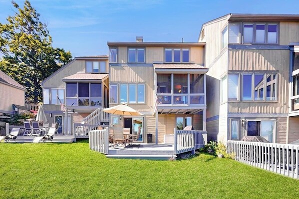 Ein mehrstöckiges Wohngebäude mit überdachter Terrasse, Sitzgelegenheiten im Freien und einem weißen Zaun.
