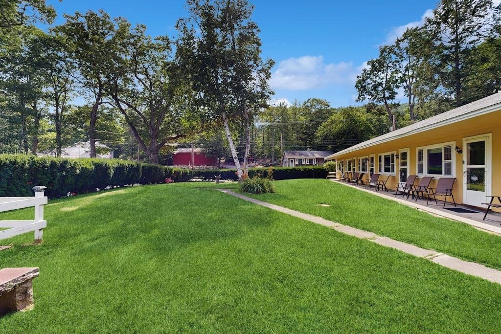 A well-maintained lawn with a white fence, a row of outdoor seating, and a building with multiple windows.