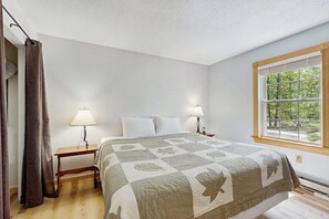 Ein Schlafzimmer mit einem Bett, zwei Nachttischen, einem Fenster mit Blick auf Grünflächen und einem Vorhang.