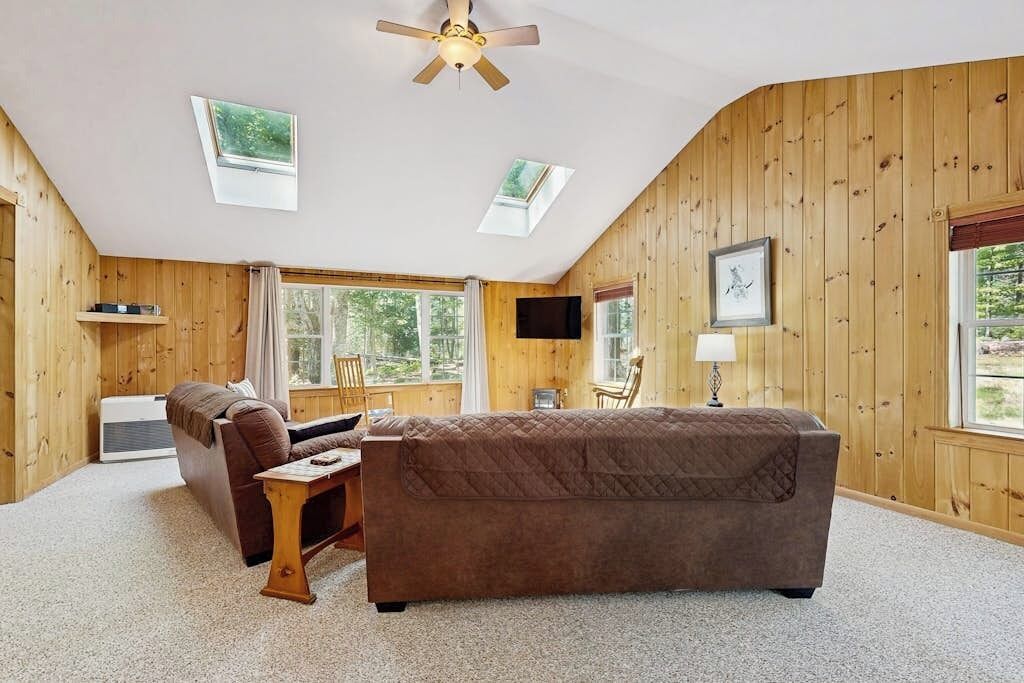 A cozy room with a brown sofa, a wooden coffee table, a ceiling fan, and a TV mounted on the wall.