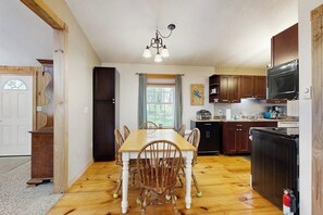 Una cocina con una mesa de comedor, sillas, armarios de madera, un refrigerador, un microondas y un televisor.