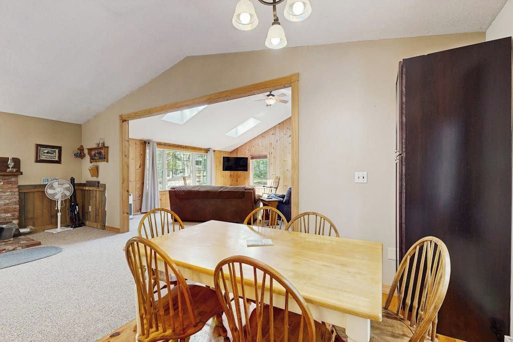 Un coin repas avec une table et des chaises en bois, un ventilateur de plafond et une vue sur l’extérieur par une porte ouverte.