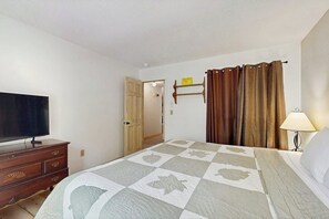Ein Hotelzimmer mit einem Bett, einem Fernseher auf einer Holzkommode, einer Lampe und einer Tür zu einem weiteren Raum.