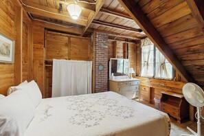 Ein Zimmer in einer Holzhütte mit einem Bett, einem Schminktisch, einem Spiegel und einem Ventilator.