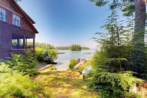 Ein Haus mit überdachter Veranda mit Blick auf einen See, umgeben von üppiger Vegetation.