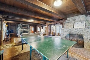 A room with a ping pong table, stone fireplace, and rustic wooden beams. - Quintessential 4BR Lakefront-Dock (Meredith)