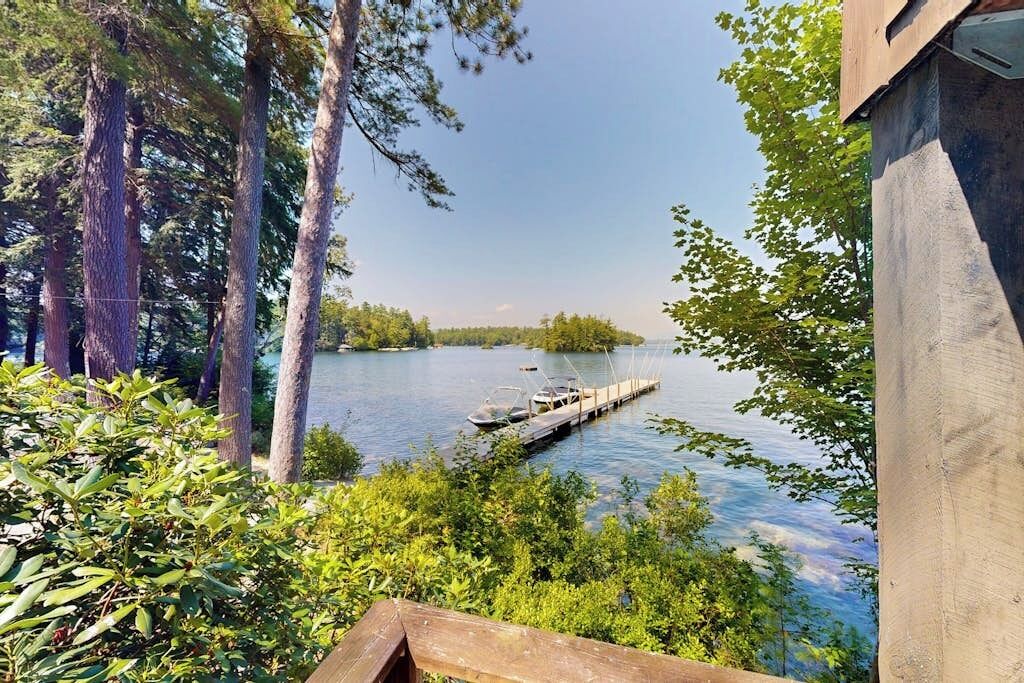 A lakeside view with docked boats, surrounded by dense greenery and tall trees.