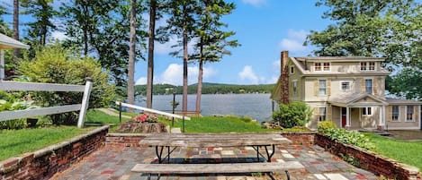 A lakeside property with a patio, a wooden bench, and a house with a chimney.