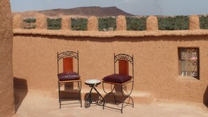 A terrace with two chairs and a small table, overlooking a desert landscape with distant hills.