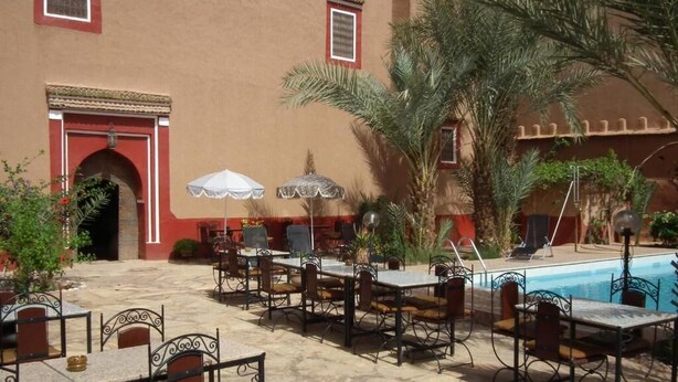 An outdoor patio with tables and chairs, a pool, and palm trees.