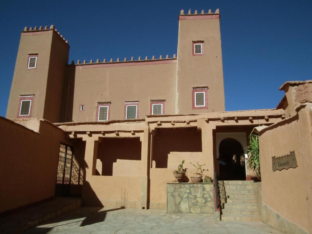 A building with a central tower and two smaller towers, a gate, and a small entrance with a potted plant.