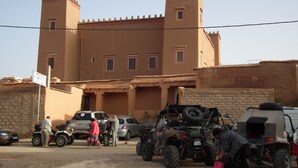 A building with a flat roof and two towers, surrounded by parked vehicles including ATVs and cars.