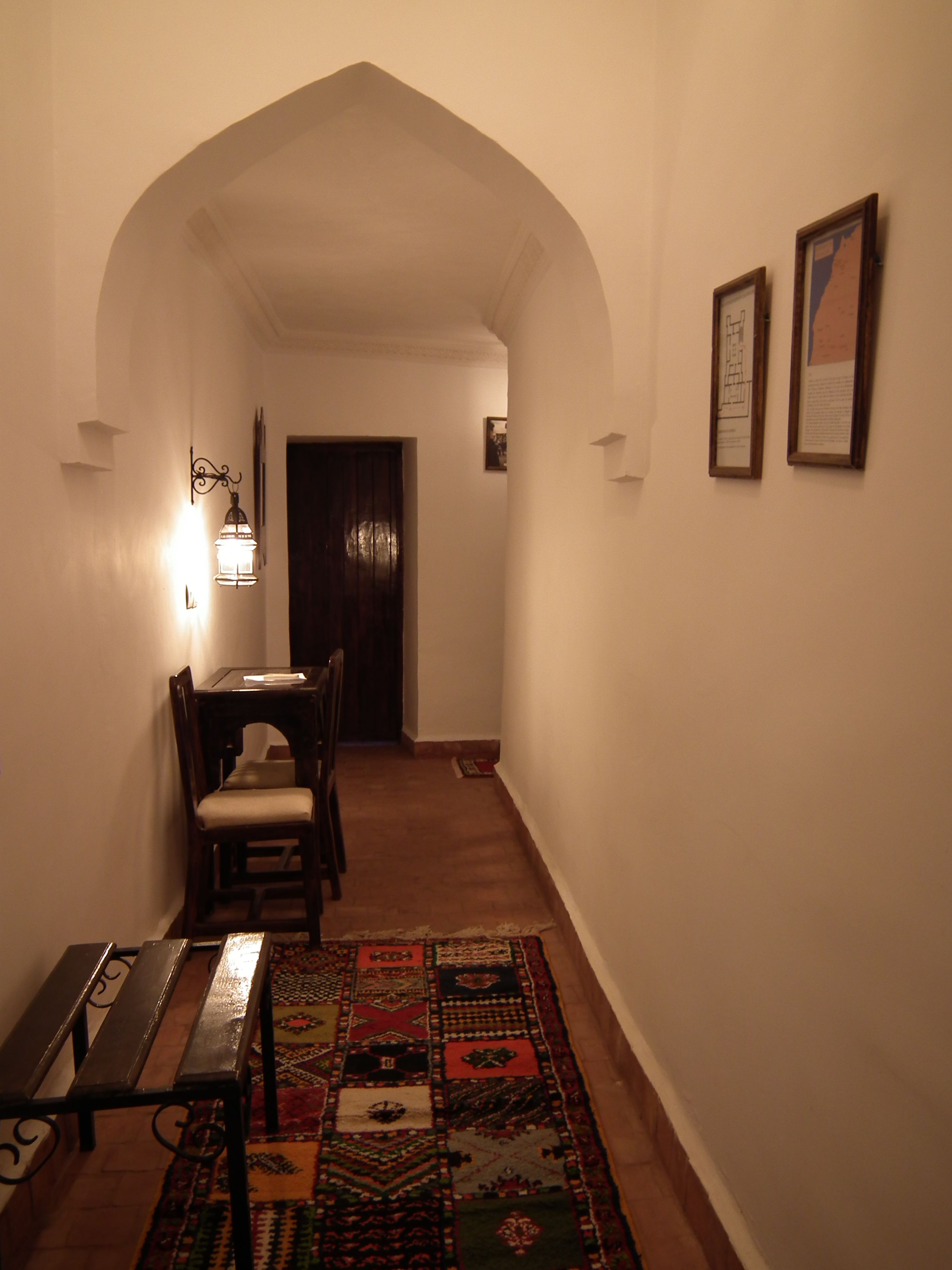 Un pasillo con un banco de madera, una mesa y sillas, que conduce a una puerta oscura.