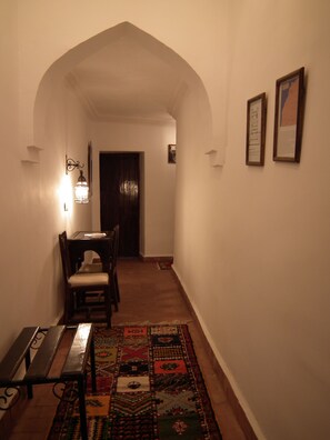 Un pasillo con un banco de madera, una mesa y sillas, que conduce a una puerta oscura.
