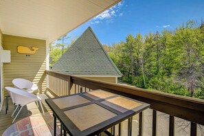 A balcony with a table and chairs, a wooden railing, and a view of trees. - Conveniently located 1BR 2nd-Floor - Deck (Gilford)