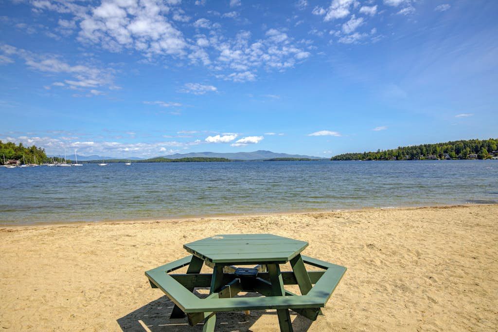 A beach with a green picnic table and a clear view of the lake and distant mountains.