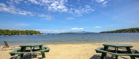 A beach with two picnic tables and a lounge chair.