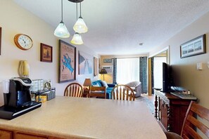 A cozy living room with a dining area, a coffee machine, a television, and a clock on the wall. - Conveniently located 1BR 2nd-Floor - Deck (Gilford)