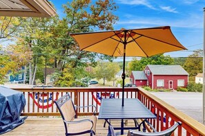 A deck with a table and chairs, an umbrella, and a railing with flags. - 4BR charming central cottage, walk to lake & town (Alton)