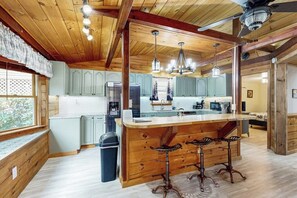 A kitchen with wooden beams, a central island with bar stools, and a view of the outdoors through a window.