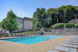 A swimming pool with lounge chairs, a stone wall, and a building in the background. - Charming 2BR Lakeview 2nd-floor - Balcony - Pool (Laconia)