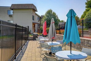 An outdoor patio area with round tables and chairs, a black metal fence, and umbrellas. - Charming 2BR Lakeview 2nd-floor - Balcony - Pool (Laconia)