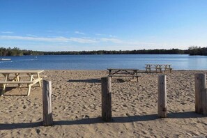 A sandy beach with wooden picnic tables and a clear view of a lake. - 3BR Near the Beach - Deck - Tennis - Washer Dryer (Moultonborough)