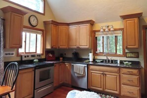Une cuisine avec des meubles en bois, une cuisinière, un lave-vaisselle et une fenêtre avec des stores.