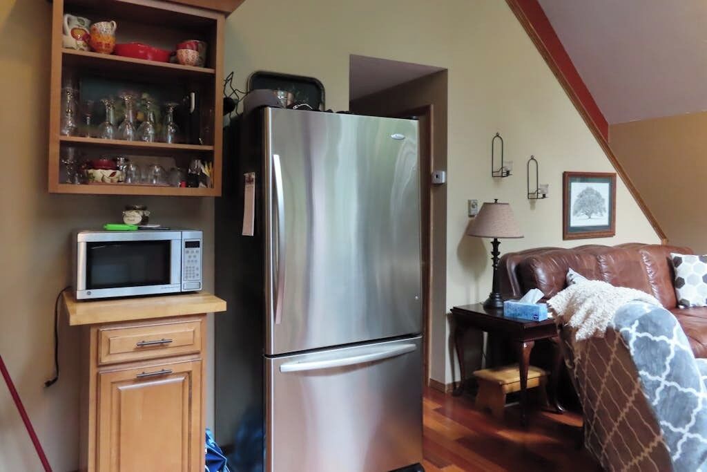 Een compacte keuken met een roestvrijstalen koelkast, een magnetron op een houten kast, en een eethoek met een leren bank in bruin.