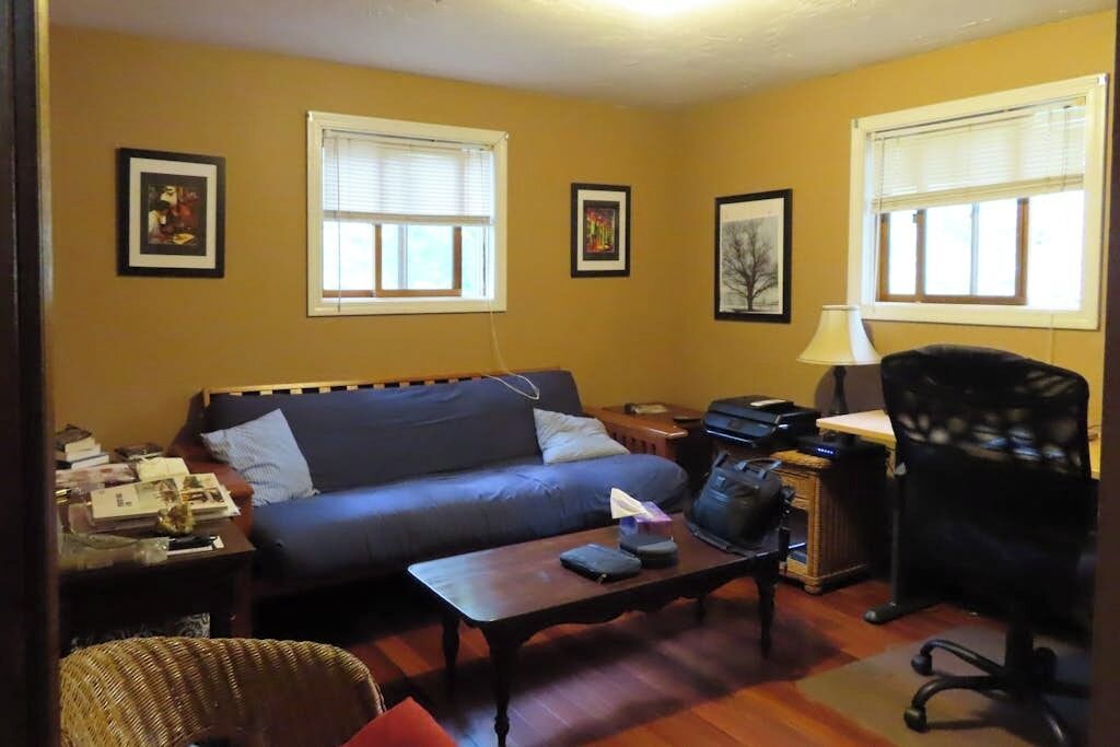 A living room with a sofa, a coffee table, a lamp, and a computer desk.