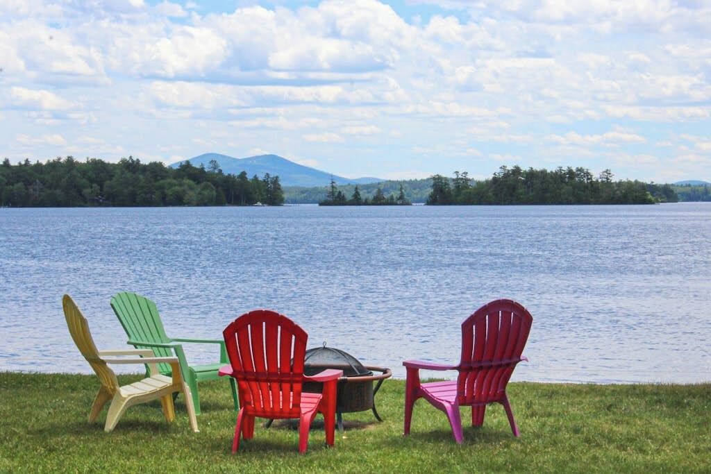 Vista del lago con tres sillas Adirondack y un brasero.