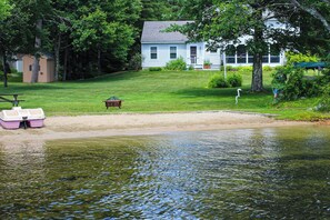 Ein Anwesen am Seeufer mit Sandstrand, einem Steg mit Boot und einem Haus im Hintergrund.