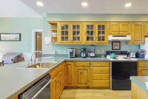 A kitchen with wooden cabinets, a dishwasher, a stove, and a coffee maker. - Stunning 3BR Lakefront - Dock - Deck - Washer Dryer (Moultonborough)