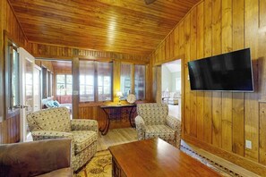 A wooden-paneled room with a TV mounted on the wall, two patterned armchairs, a wooden table, and a window with a view. - Stunning 3BR Lakefront - Dock - Deck - Washer Dryer (Moultonborough)