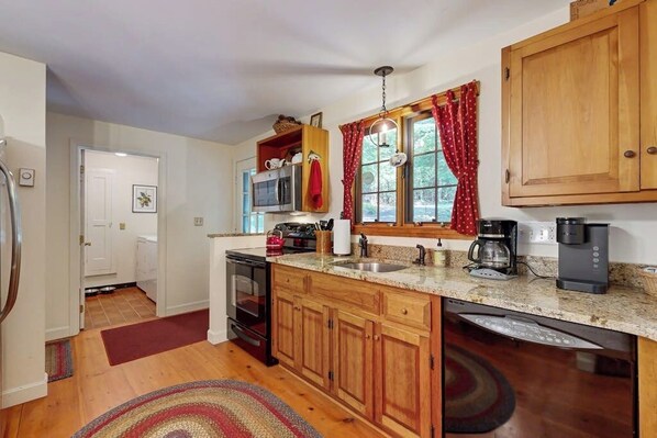 A kitchen with wooden cabinets, a microwave, a coffee maker, and a dishwasher. - Picturesque Squam Lake House: beach and dock access (Center Harbor)