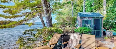 Une terrasse en bois, dotée de chaises longues et d’une petite construction, qui offre une vue sur une étendue d’eau.