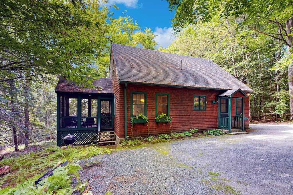 Un chalet rustique doté d’une véranda, entouré d’une forêt dense.