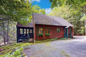 A rustic cabin with a porch, surrounded by dense forest. - Picturesque Squam Lake House: beach and dock access (Center Harbor)