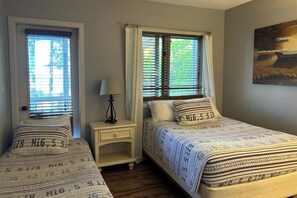 A bedroom with two single beds, a nightstand with a lamp, and a painting on the wall.