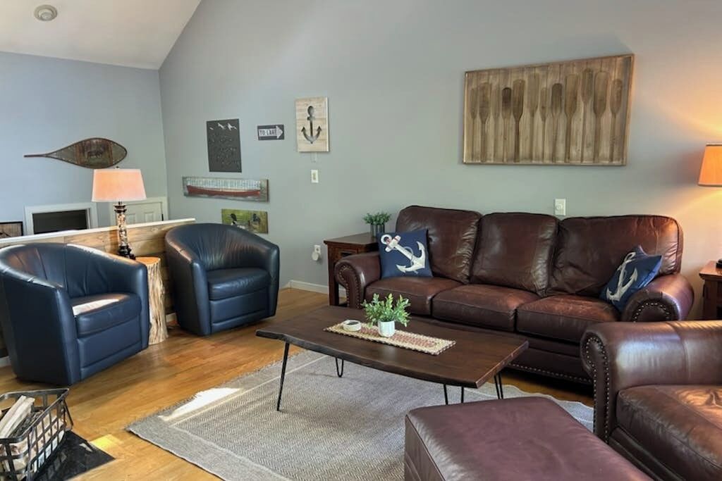 Ein Wohnzimmer mit einem braunen Ledersofa, zwei blauen Sesseln, einem Couchtisch und einem hölzernen Wandbild.