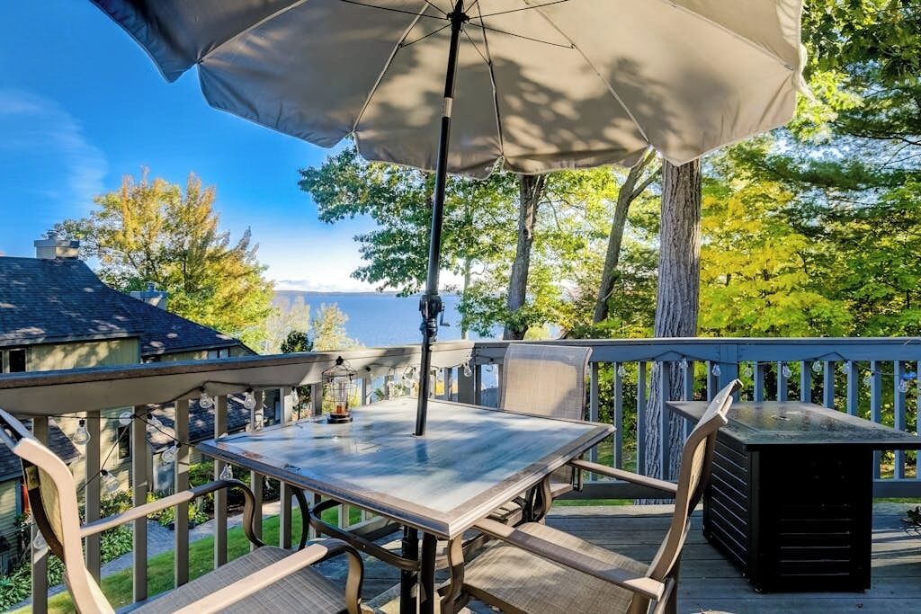 An outdoor deck with a table and chairs, a large umbrella, and a view of trees and a building.