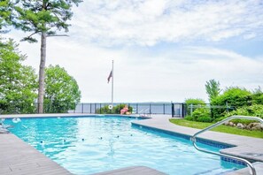 A swimming pool with a flagpole, surrounded by a fence and greenery.