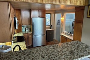 A compact kitchen with wooden cabinets, a stainless steel refrigerator, granite countertops, and a window providing natural light.