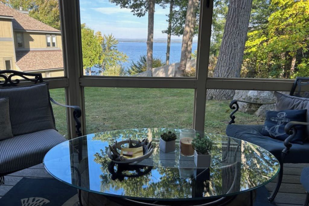 A glass-enclosed patio with a round table, two chairs, and a view of the sea.