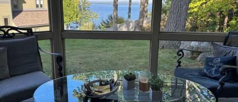 A glass-enclosed patio with a round table, two chairs, and a view of the sea.