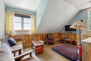 A cozy loft-style room with a wooden ceiling, a sofa, a small table, a chair, a television, and a window with curtains. - Captivating 3BR Lakefront - Washer Dryer (Meredith)