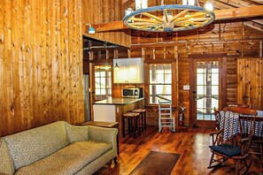 A log cabin interior with a wooden floor, a sofa, a dining table with chairs, a kitchen area with a microwave, and a large wooden ceiling fan. - Cozy 2BR Dog Friendly - Beach Down the street (Moultonborough)