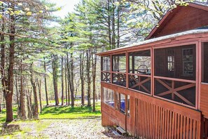 Uma cabana com varanda e vista para uma área arborizada.